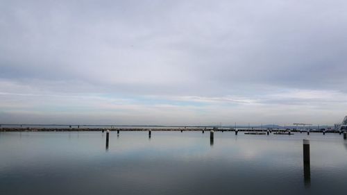 View of bridge over calm sea against cloudy sky