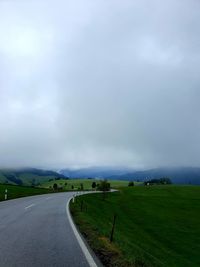 Empty road amidst field against sky