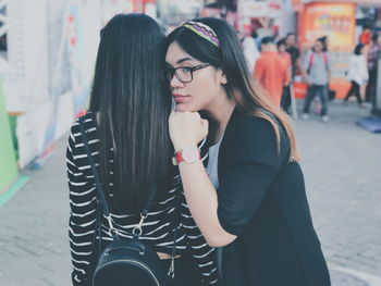 Side view of young woman leaning on female friend at street