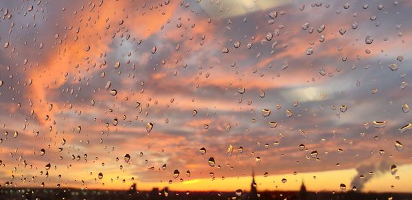 Full frame shot of wet glass window against sky during sunset