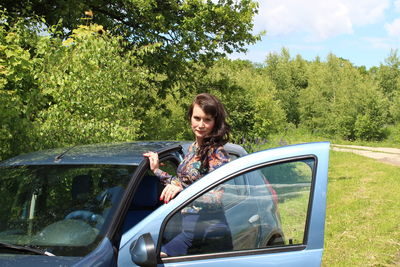 Portrait of woman standing by car on field