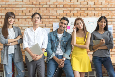 Portrait of colleagues standing against brick wall at office