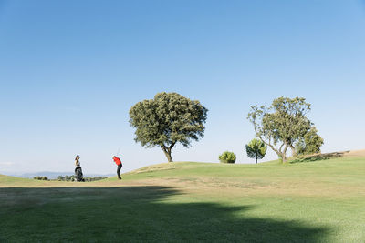 People on golf course against clear sky