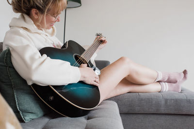 Woman sat on the couch playing guitar smiling