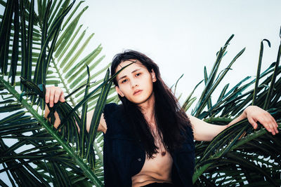 Close-up of young woman with palm tree against sky