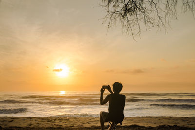 Silhouette man sit on beachchair during record vdo and photo beach with sunrise and sea background