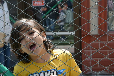 Close-up portrait of boy looking through chainlink fence