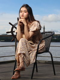 Portrait of young woman sitting on chair against lake