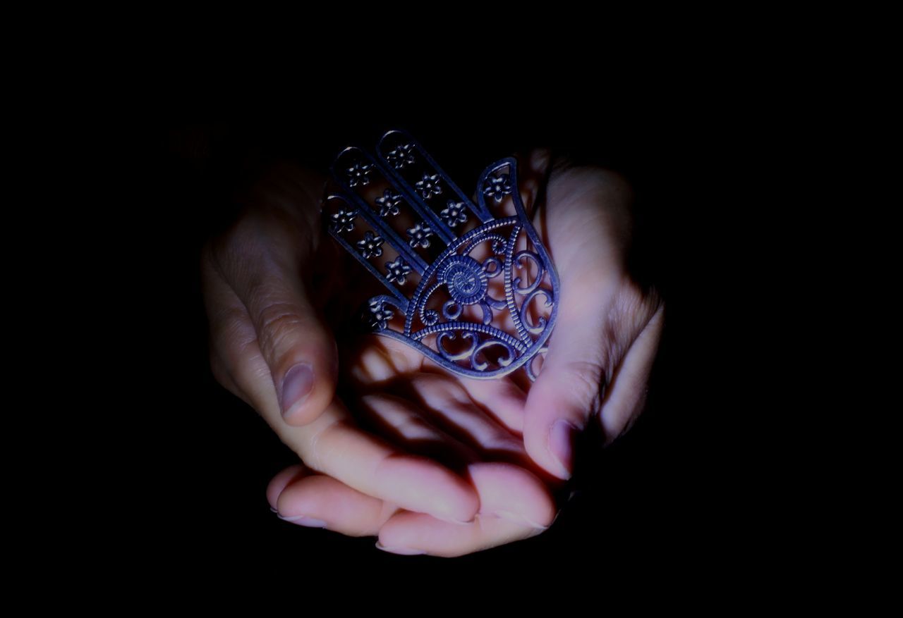 CLOSE-UP OF HAND HOLDING HANDS AGAINST BLACK BACKGROUND