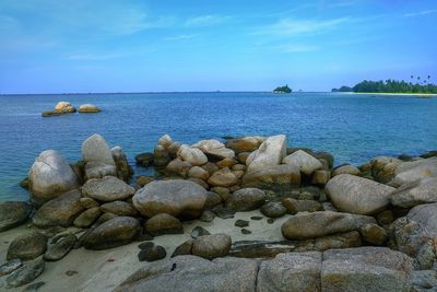 Scenic view of rocky shore and sea against blue sky