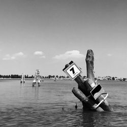 Wooden post falling in sea against sky