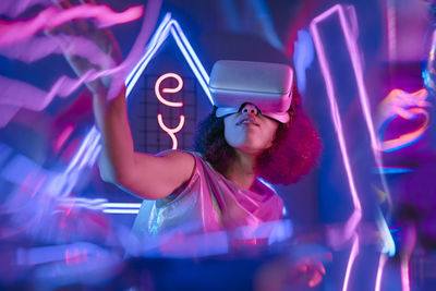 Woman wearing virtual reality simulator in glowing neon light room