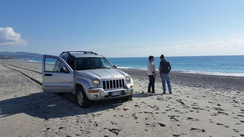 Rear view of people standing on beach against clear sky