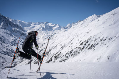 Young man with ski makes pose in mountains behind