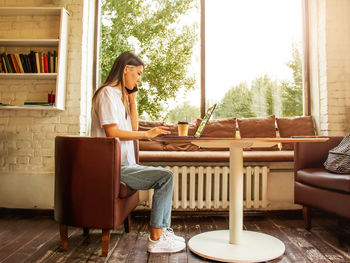 Young asian woman sitting at a table in a cafe working in a laptop, a table in a cafe by the window