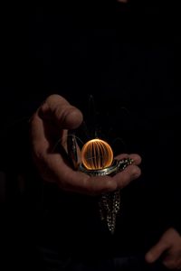 Cropped hands of man holding pocket watch with wire wool against black background