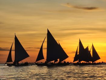 Silhoutted sailboats sailing on sea against sky during sunset