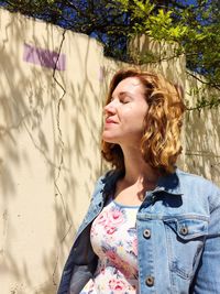 Young woman with closed eyes against wall on sunny day