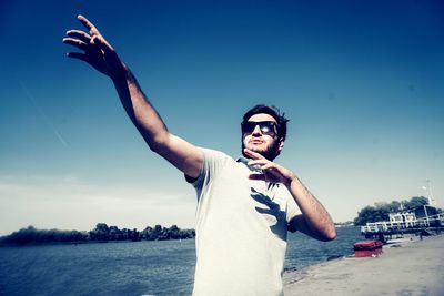 Young man wearing sunglasses while standing at beach against sky