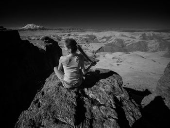 Rear view of woman sitting on rock against sky