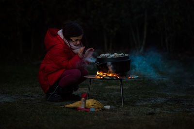 Girl crouching by barbecue grill on field