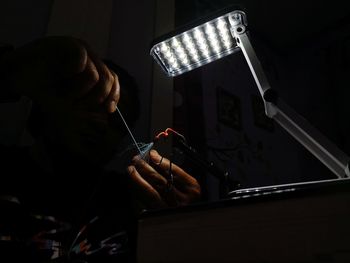 Close-up of hands holding equipment by illuminated lamp in darkroom