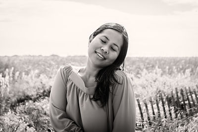 Young woman with eyes closed standing on field against sky