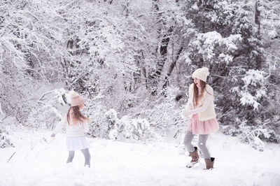 Funny kid girl playing with snow throw snowballs at each other wearing knitted sweaters and skirts.