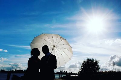 Silhouette couple with umbrella standing against sky during sunny day