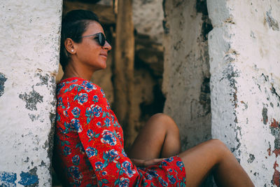 Young woman looking away while sitting on wall