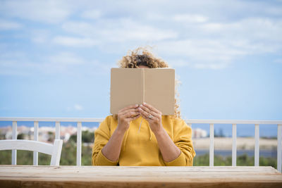 Portrait of person hiding behind railing against sky