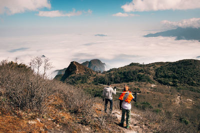 Rear view of men standing on mountain against sky