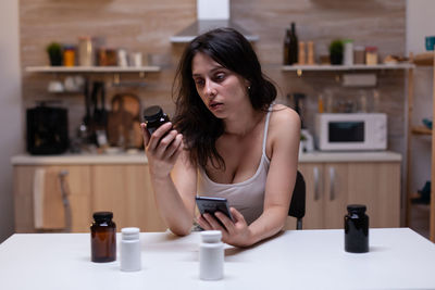 Young woman holding mobile phone and bottle at home