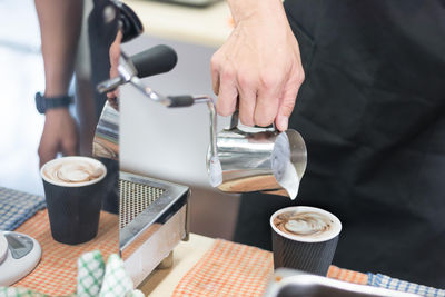 Midsection of person pouring milk in coffee cup