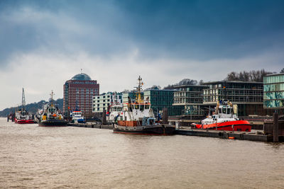 Boats moored at harbor against sky in city