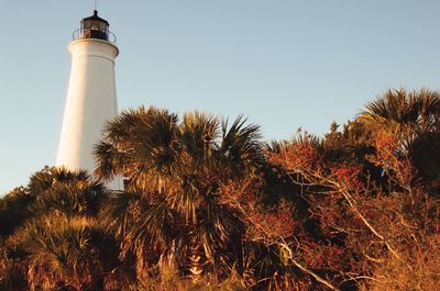 Lighthouse by trees against clear sky