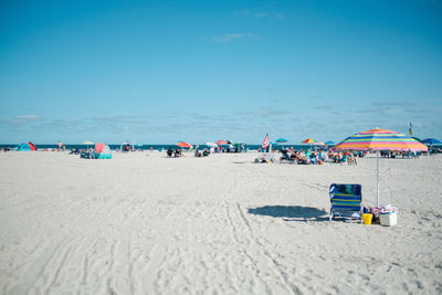 Lounge chairs and parasols on beach against blue sky