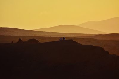 Scenic view of people on desert against sky during sunset