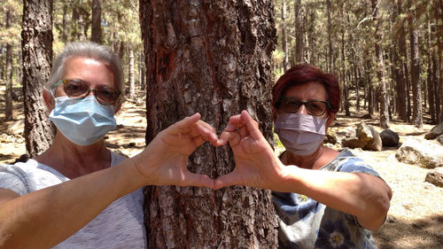 Portrait of friends wearing sunglasses and mask on tree trunk in forest