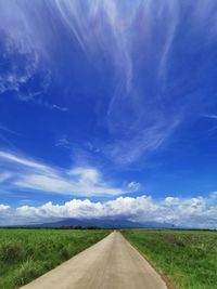 Empty road amidst field against blue sky