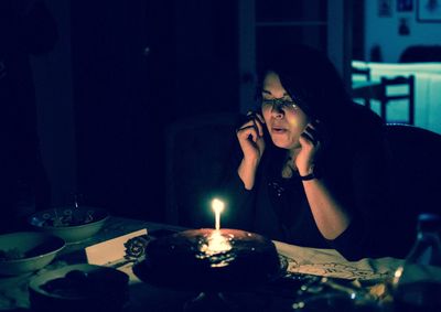 Woman blowing candle on cake in darkroom at home