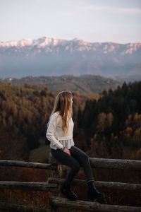 Beautiful blonde woman relaxing on the fence in the mountains at sunset. vacation travel,concept.