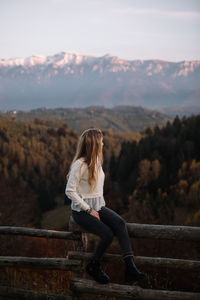 Woman sitting on railing against mountain