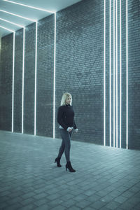 Full length of woman walking against illuminated lights on wall