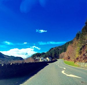 Road leading towards mountains against blue sky