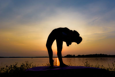 Silhouette woman and girl practicing yoga against sky during sunset