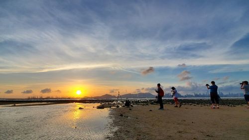 People on beach against sky during sunset