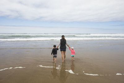 Rear view of mother walking toward ocean holding hands of her two kids