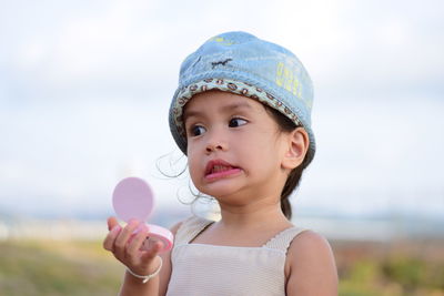 Close-up girl holding hand mirror against sky