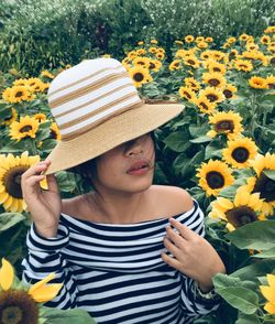 Woman wearing hat standing amidst sunflowers